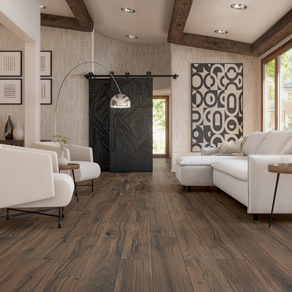 Living room with floor tile that looks like dark wood planks, off-white glossy wall tile, wood barndoor on slider, silver floor lamp, white sofa and side chairs.
