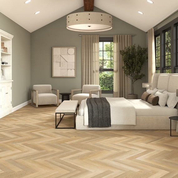 Transitional bedroom with LVT wood look floor tile in herringbone pattern, muted green walls, white platform bed, upholstered bench and side chairs.