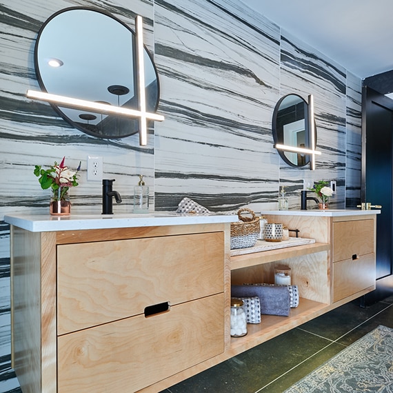 Floating bathroom vanity with bold cream & black backsplash, round mirrors with integrated lighting, white quartz counter, natural wood cabinets.