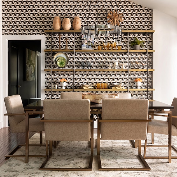 Dining room with table & chairs and feature wall with floor-to-ceiling white, gray & black mosaic tile and brass shelving.