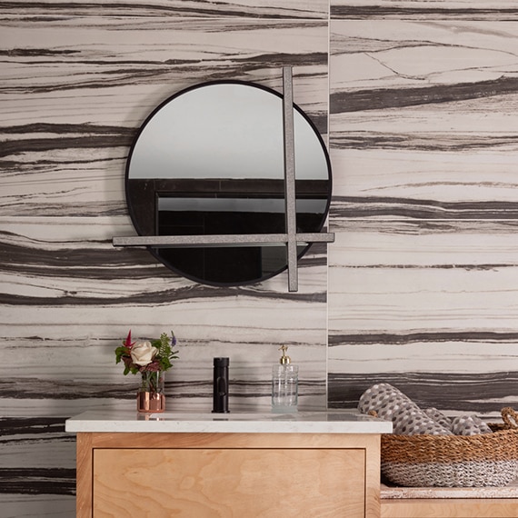 Bathroom vanity with bold cream & black backsplash, round mirror with integrated lighting, white quartz counter, natural wood cabinet.