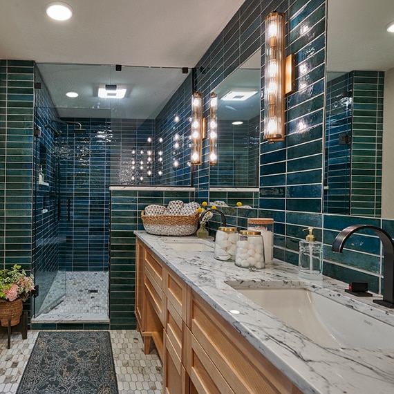 Bathroom with teal glazed porcelain wall tile, marble countertop, natural wood cabinets, elongated hex mosaic marble floor tile.