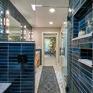 Shower with blue glazed porcelain wall tile, marble shelves & bench, brass & glass sconces, elongated hex mosaic marble floor tile.