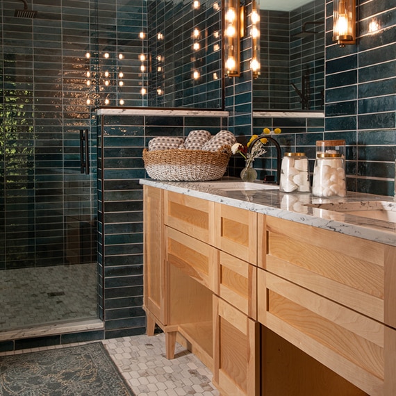 Bathroom with teal glazed porcelain wall tile, marble countertop, natural wood cabinets, elongated hex mosaic marble floor tile.