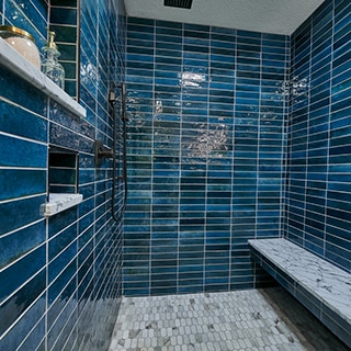 Shower with blue porcelain wall tile, bench of white & gray marble slab, marble elongated hex mosaic shower floor tile.