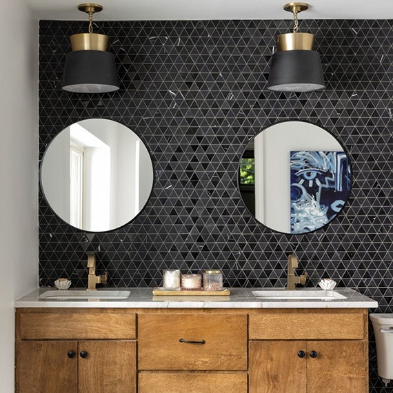 Renovated bathroom with woodgrain vanity, gray natural quartzite counter with two sinks, round mirrors on black natural stone triangle mosaic backsplash.