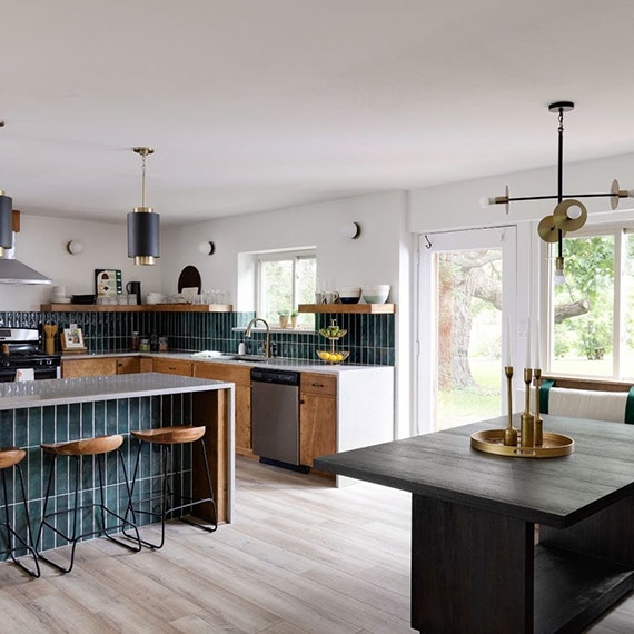 Renovated kitchen with gray quartz countertops & waterfall island, teal glossy backsplash, woodgrain floating shelves and cabinets, banquette with wood table.