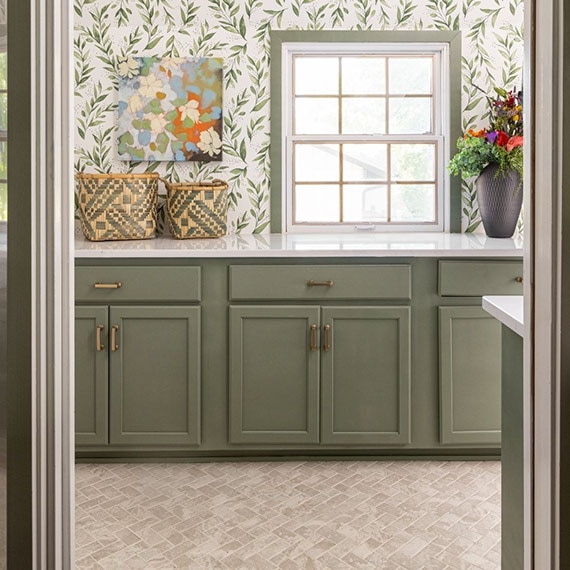 Renovated pantry with white quartz countertops, wallpaper with green leaf graphics, olive cabinets, and beige stone look herringbone floor tile.