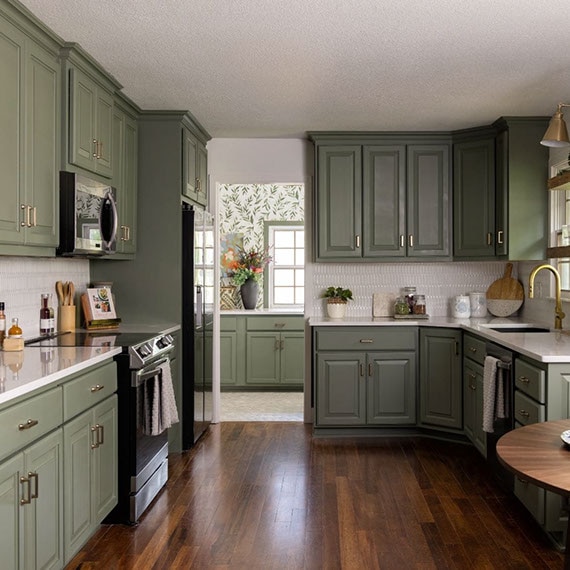 Renovated kitchen with white quartz countertops, white picket mosaic tile backsplash, olive cabinets, and floating woodgrain shelves.