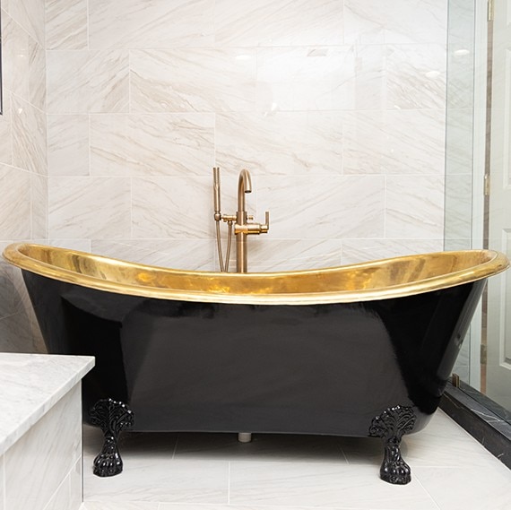 Renovated bathroom wet room with black & gold soaker tub, white & gray marble look shower wall and floor tile.