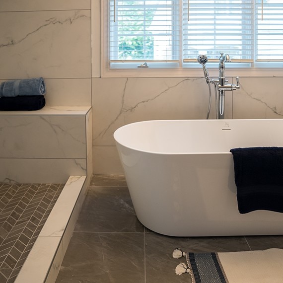 Renovated bathroom with soaker tub, white & gray marble look wall tile, dark gray marble look tile floor, and dark gray marble look mosaic shower floor tile.