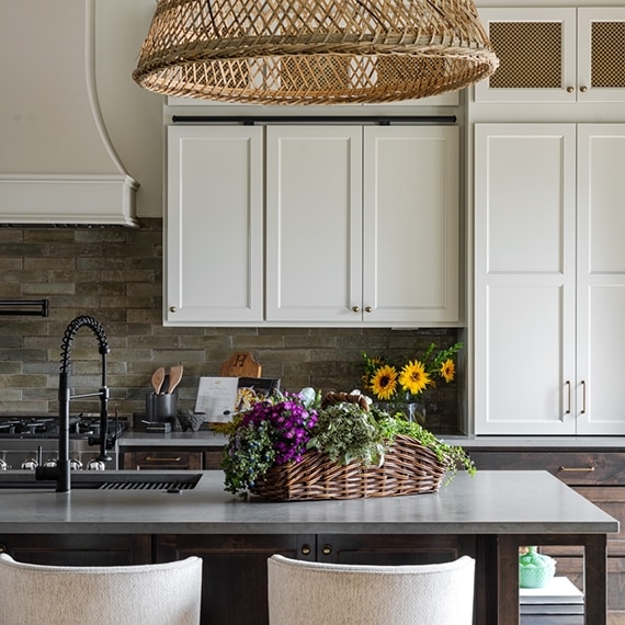 Renovated kitchen with off-white cabinets, glossy brown subway tile backsplash, gray quartz countertops, island with sin and basket pendant lighting.