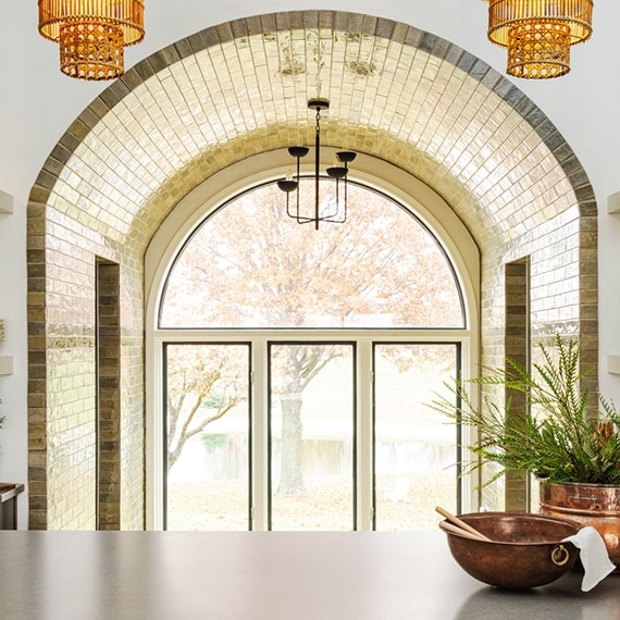 Renovated kitchen with gray quartz island countertop and arched entryway covered by glossy brown tile.