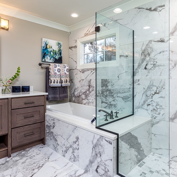 Renovated bathroom featuring white & gray veined porcelain slab that looks marble slab on the wall, tub surround, and shower walls.