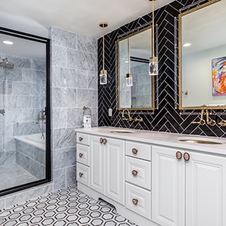 Renovated bathroom with black herringbone tile backsplash, vanity with dual sinks, black & white marble hexagon floor tile, and wet room with marble floor and wall tile.