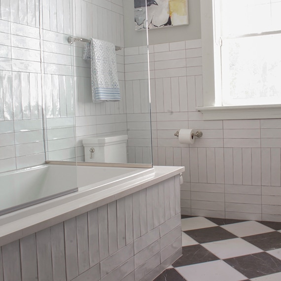 Bathroom with black and white marble checkered floor tile, wall and tub surround covered with white ceramic tile in a basketweave pattern.