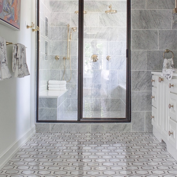 Renovated bathroom with black & white hexagon floor tile, wet room with gray marble wall tile and mosaic floor tile, and polished brass fixtures.