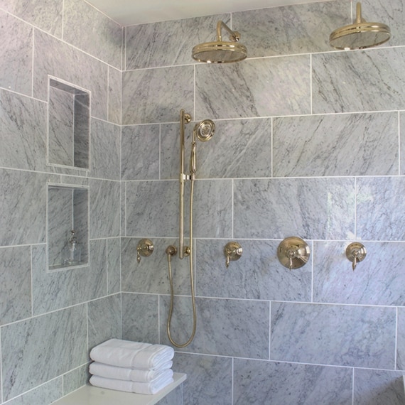 Elegant shower with large format gray marble with white marble bench, two shower niches, brass showerheads and brass fixtures.