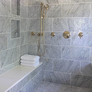 Renovated bathroom with wet room of gray marble wall tile, marble mosaic floor tile, and polished brass fixtures.