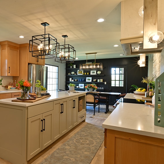 Remodeled kitchen with off-white quartz countertops, wood upper and gray lower cabinets, black cage pendants over island, and black feature wall in adjacent dining room.