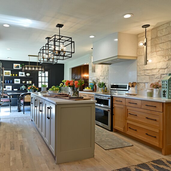 Remodeled kitchen with off-white quartz countertops, wood and gray cabinets, black cage pendants over island, and black feature wall in adjacent dining room.