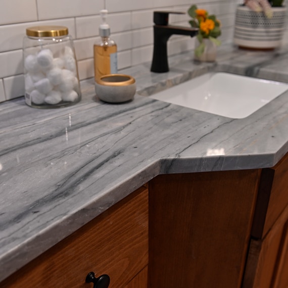 Children’s bathroom with gray quartzite countertop with heavy striations on a vanity of natural wood cabinets, and white ceramic tile backsplash.