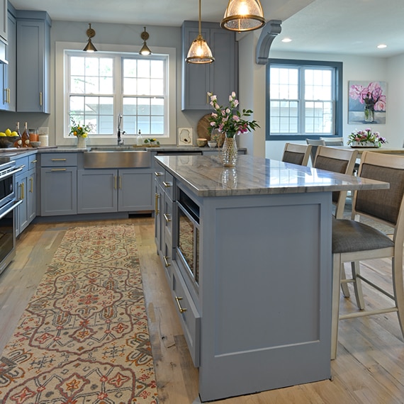 Transitional kitchen with country blue cabinets, gray quartzite with heavy striations countertops and island, stainless steel farm sink, and pendant lighting.