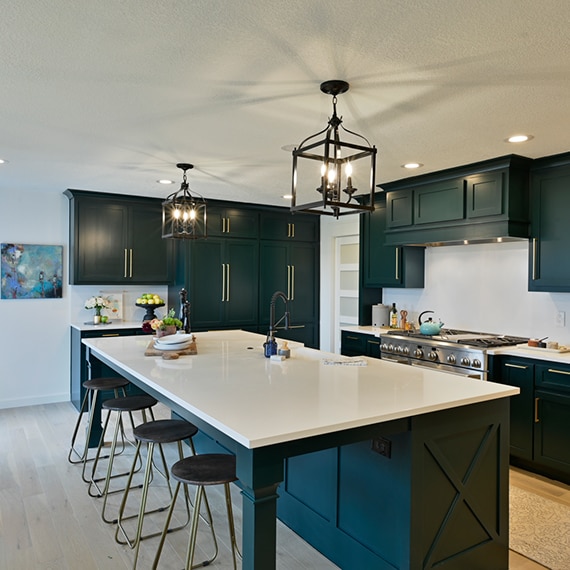 Remodeled kitchen with white quartz countertops and backsplashes, dark green cabinets with brass hardware, and black cage pendants over island.