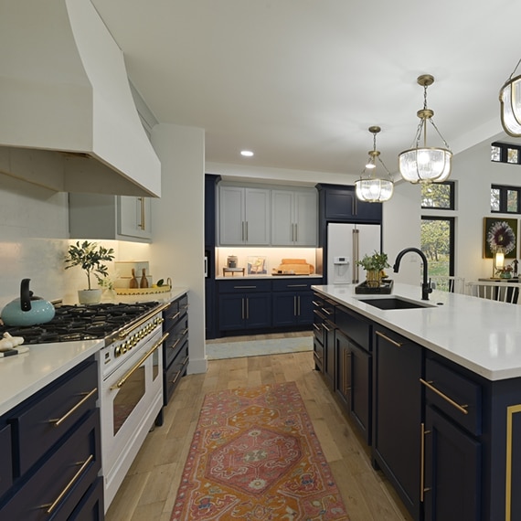 Kitchen with white upper cabinets, navy lower cabinets, white quartz countertops, island with sink, glass & brushed brass pendant lights.