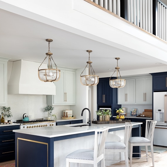 Kitchen with white upper cabinets, navy lower cabinets, white quartz countertops, island with sink, glass & brushed brass pendant lights.