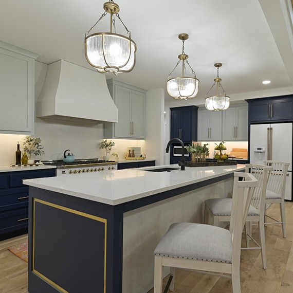 Kitchen with white upper cabinets, navy lower cabinets, white quartz countertops, island with sink, glass & brushed brass pendant lights.