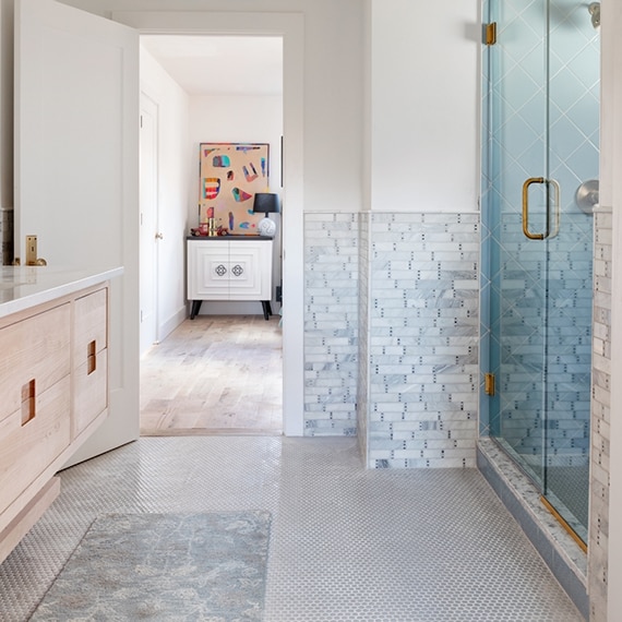 Bathroom with marble mosaic wainscoting, 6x6 blue shower tile in a diamond pattern, gray penny round tile floor, and natural wood floating cabinet.