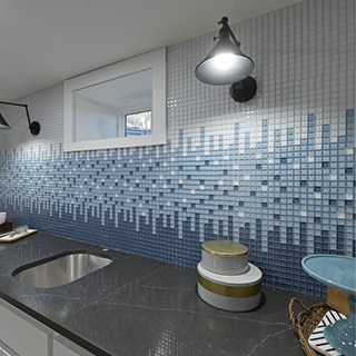 Backsplash with white, light blue, and dark blue glass mosaic tile, black quartz countertop, and basement window with lamps on each side.