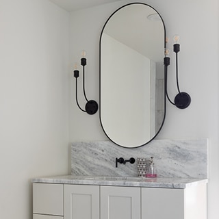 Bathroom vanity with black frame mirror between black sconces, black faucet, white & gray marble countertop over white cabinets.