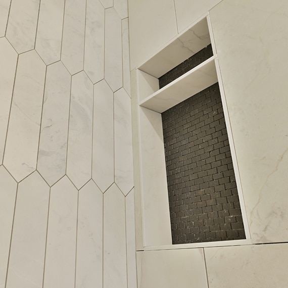 Closeup of shower walls with large, white marble tile with gray veining, marble picket tile accent, and dark gray mosaic tile in shower niche.