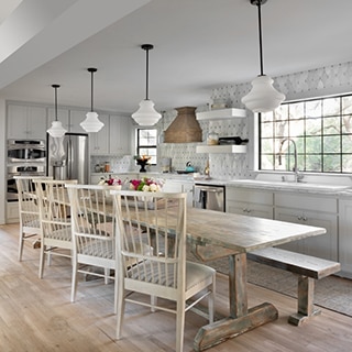 Open concept dining room and kitchen with white & gray marble countertop, antique mirror & marble mosaic backsplash, distressed wood table & chairs.