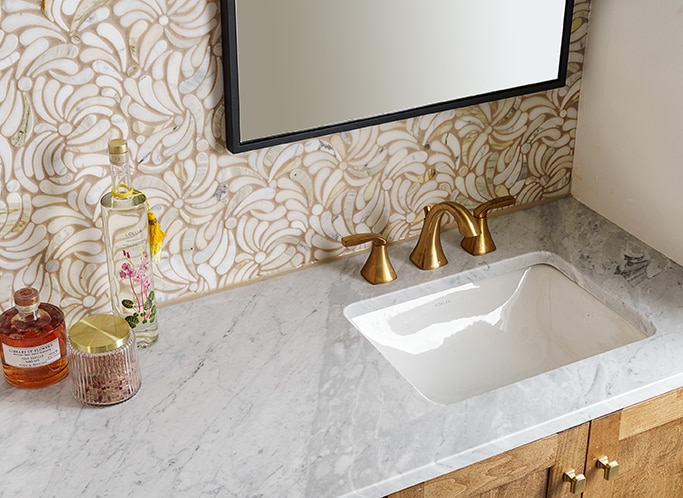 Bathroom with white marble countertop, mosaic wall, and wood cabinets.