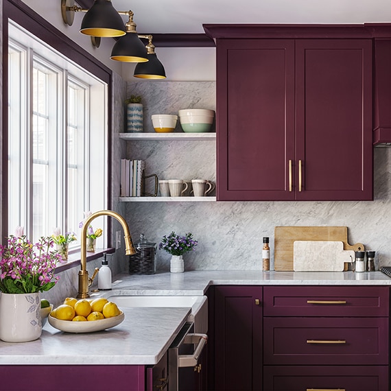 Kitchen with purple cabinets and white marble look countertops and backsplash.