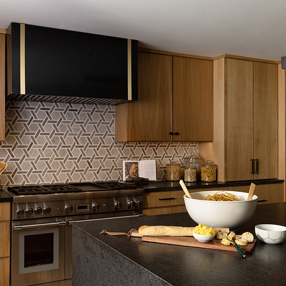 Kitchen with light wood cabinets, black countertop on center island, and a brown mosaic on the backsplash.