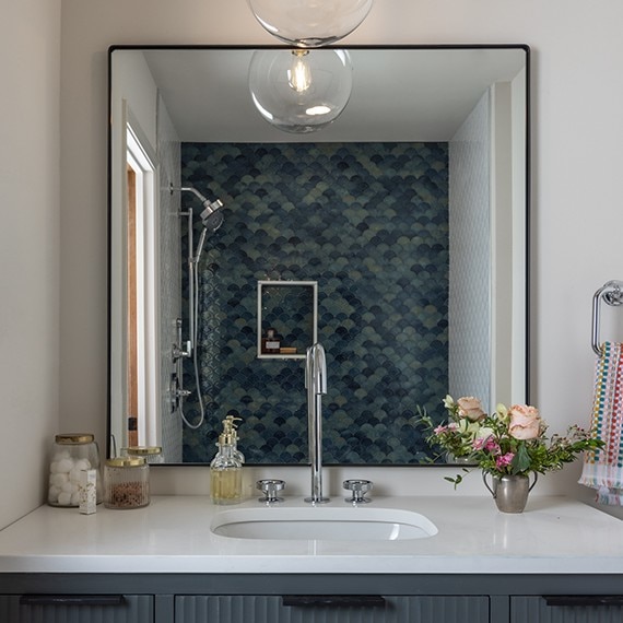 Bathroom sink with the bathroom mirror reflecting the shower, showing a blue fan mosaic tile.