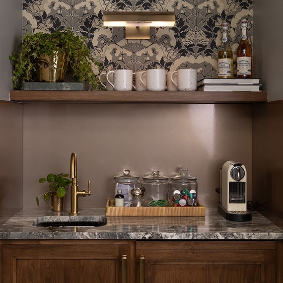 Coffee bar with brown wall, dark wood cabinets, gray marble countertop, and various coffee supplies.