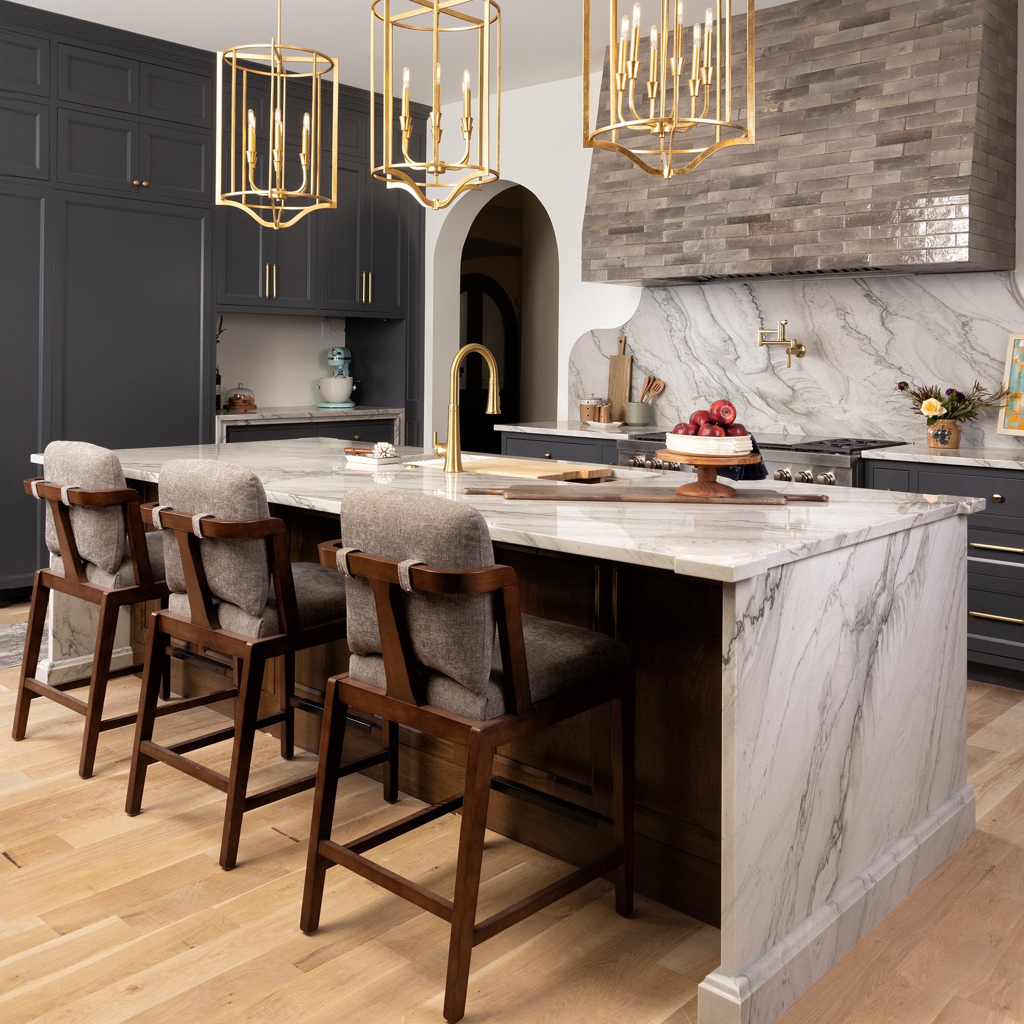 Kitchen sink island and seating area with a white marble look slab countertop and backsplash, and the vent hood covered in a gray subway tile.