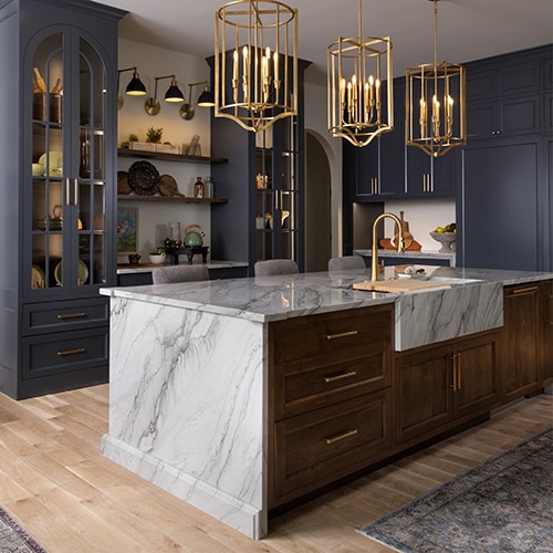 Kitchen with blue cabinets, center island with a white marble waterfall countertop, gold accents, and a light wood floor.