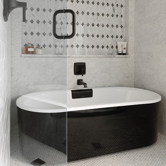 Black bathtub with white marble on the shower walls, white marble look penny round mosaic on the shower floor, and white marble look mosaic on the wall niche.