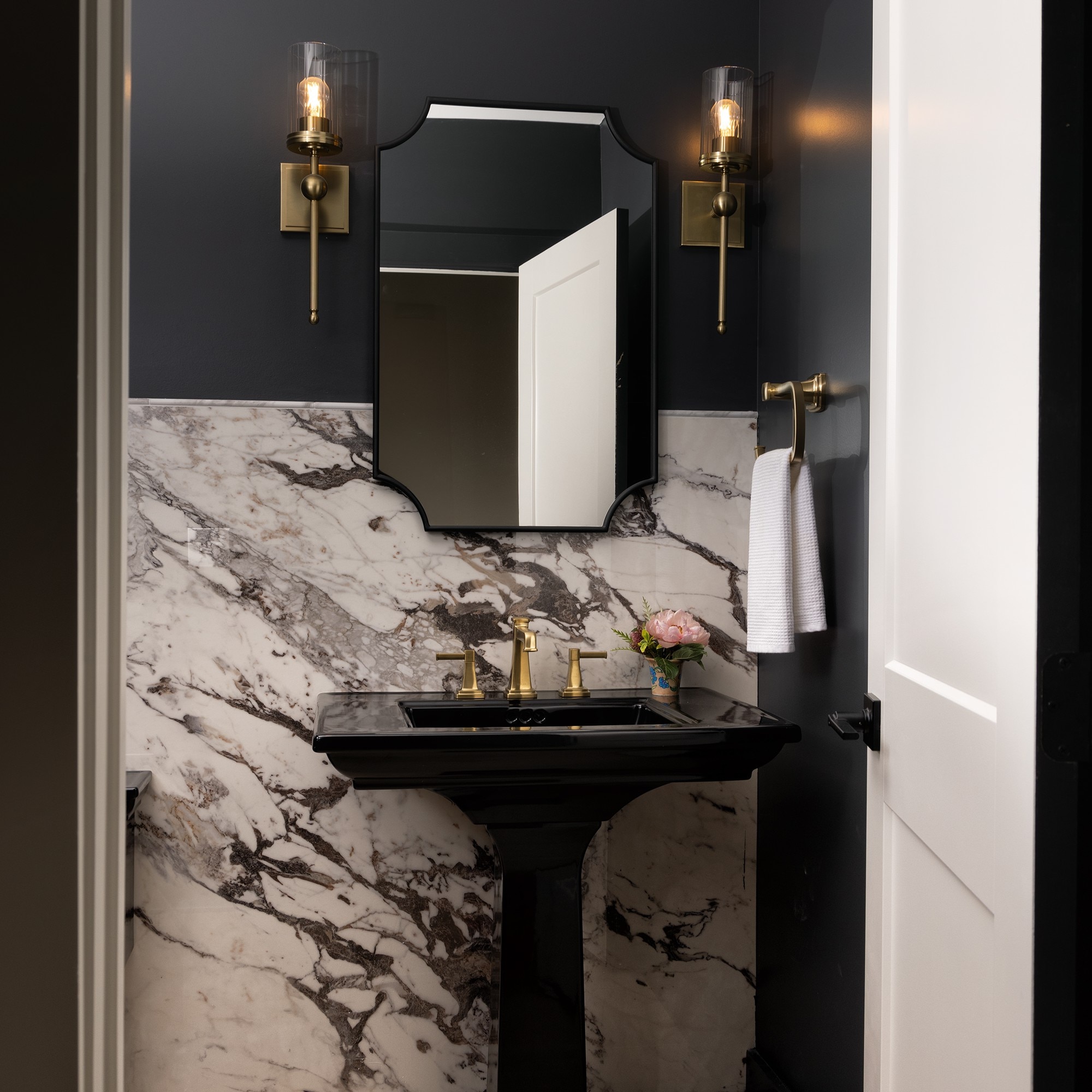 A half bath showing a vanity with a black sink and wall, gold fixtures, and a white marble slab on half the wall.