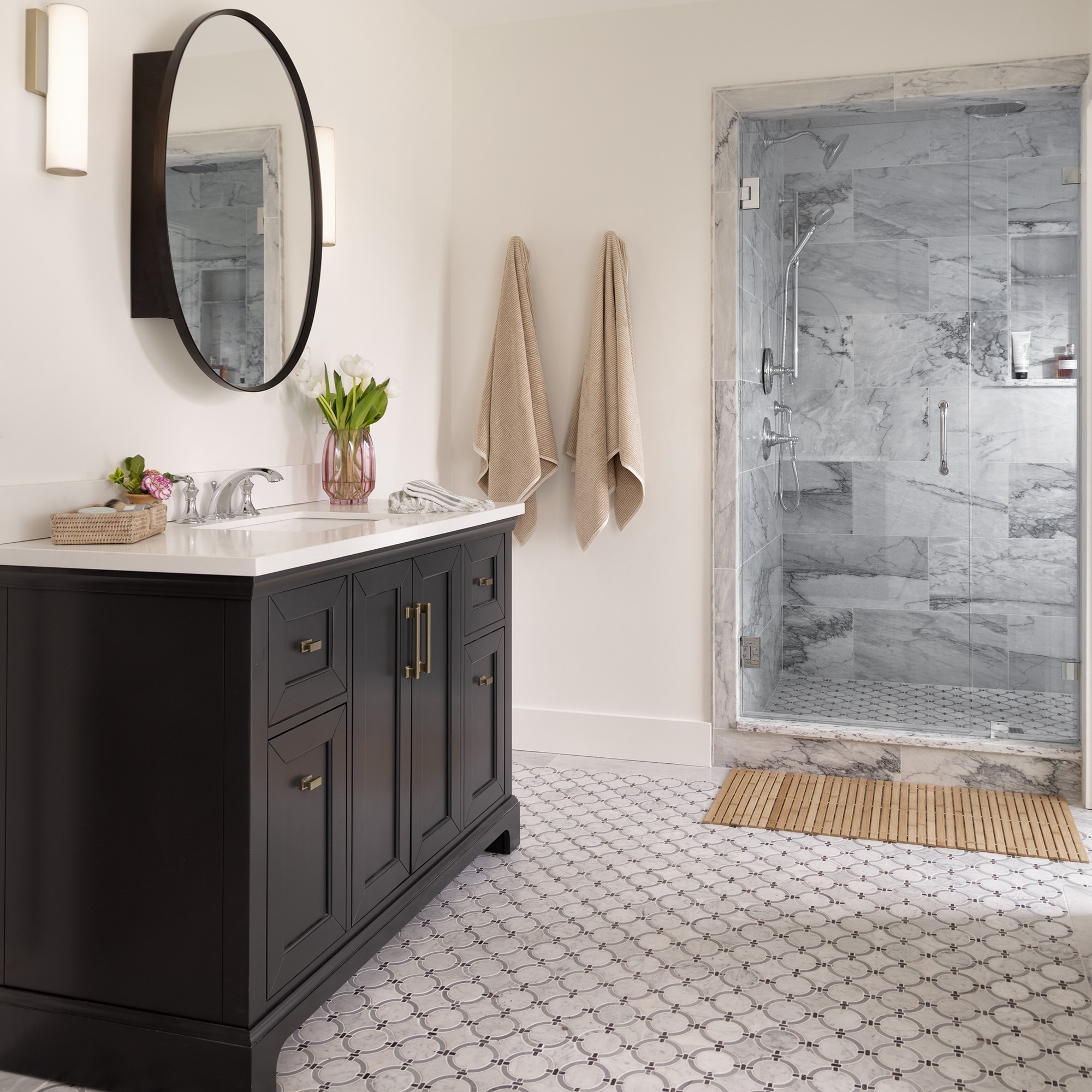 Bathroom with black cabinets, white marble look countertop, white marble look ring mosaic, and white marble shower walls.