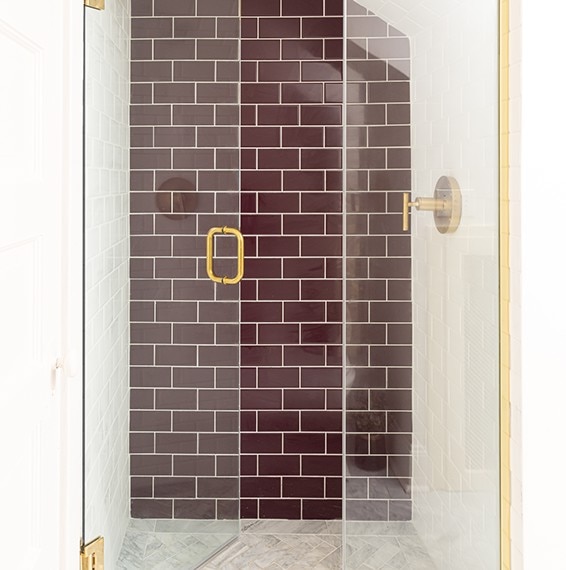 Shower with white marble herringbone mosaic floor tile, white subway tile on the shower walls, and purple subway tile on back shower wall.