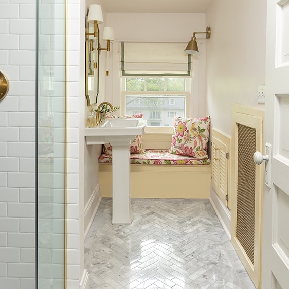Bathroom sink with white walls, sitting bench, white sink, and white marble look herringbone mosaic floor tile,.