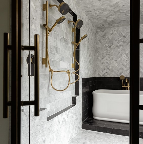 Shower with white marble herringbone mosaic on walls, white marble rectangle mosaic, white marble hexagon mosaic on the floor, and black marble look tile surrounding the tube and on the shower niches.