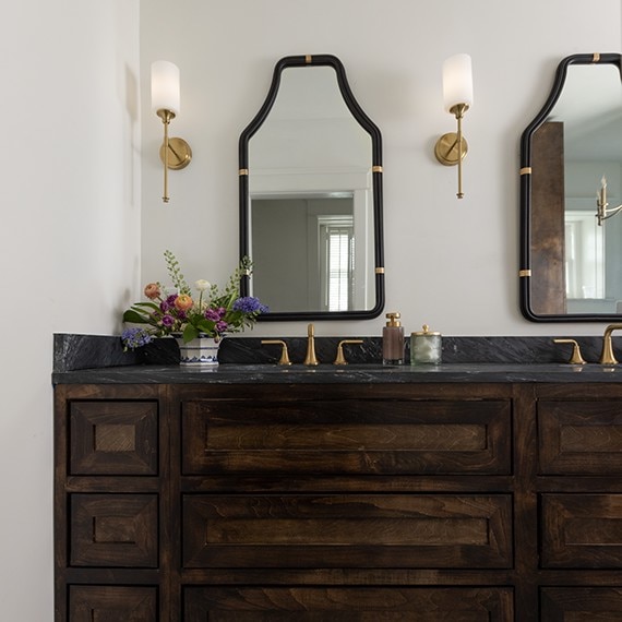 Bathroom with his and hers sinks, dark wood cabinets, gold fixtures, and black marble countertops.